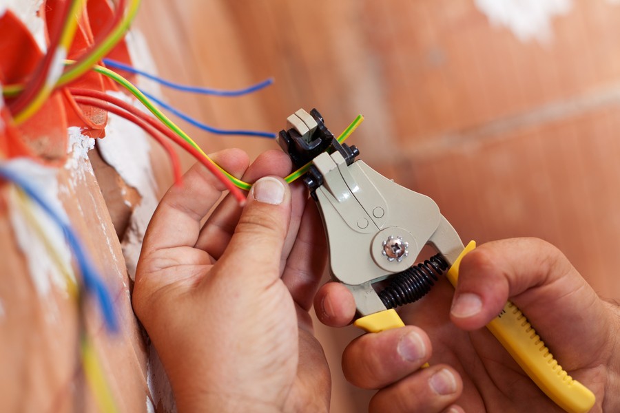 A hand holding a wire stripping and crimping tool working on wiring installation.