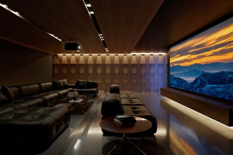 A home theater with acoustic treatments has a 4K projector displaying a mountainous landscape. 