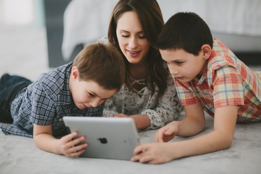 A woman and two children lying down and using a laptop.
