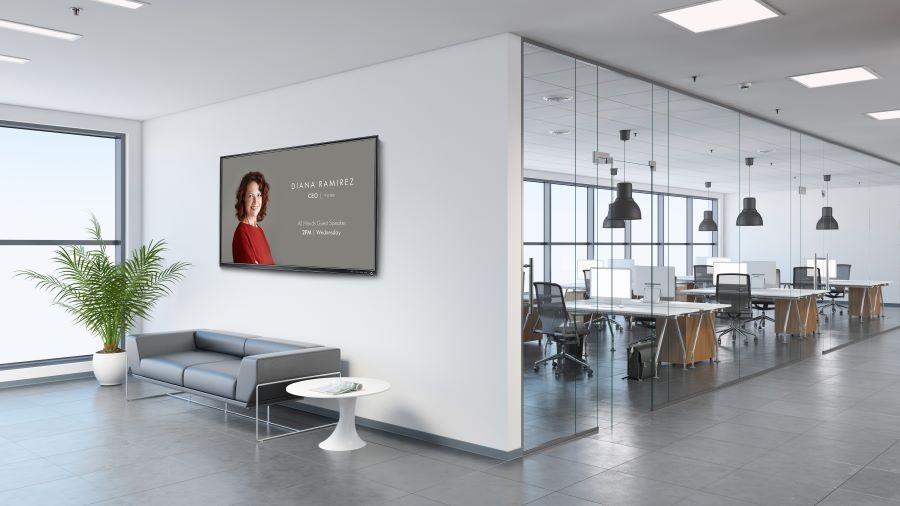 A video display on the wall of a business. In the background are multiple workstations.