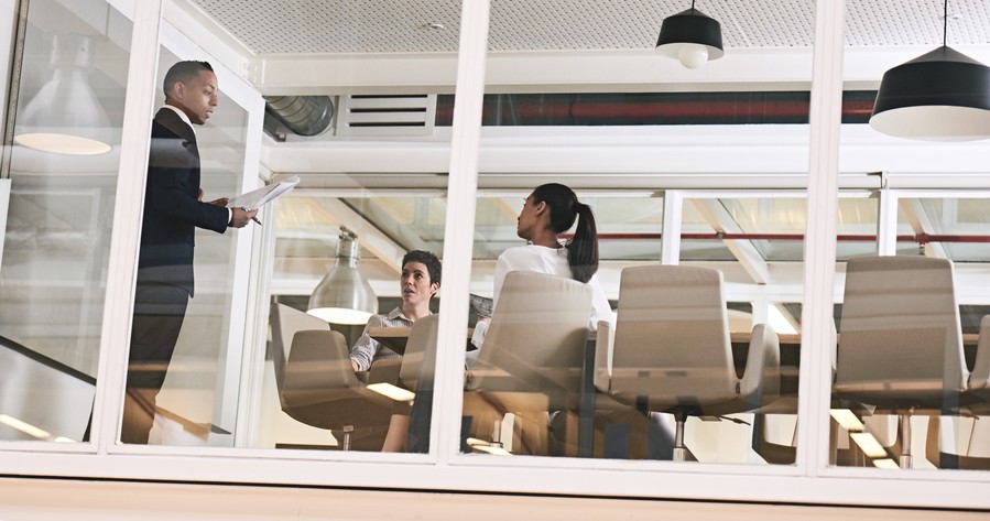 exterior view of a corporate conference room with a presenter talking to two seated employees