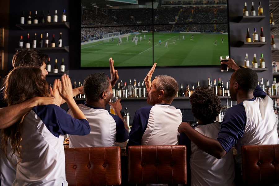 group of fans watching a soccer game on a sports bar video wall, high-fiving each other