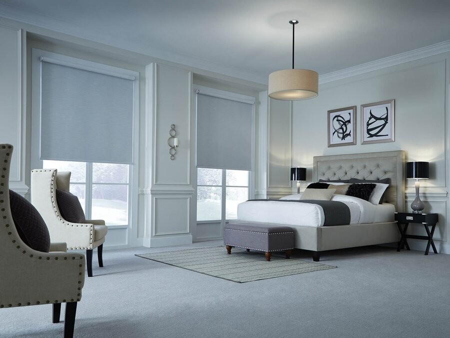 A bedroom featuring a bed, two large windows with motorized shades lowered halfway, and various lighting fixtures.