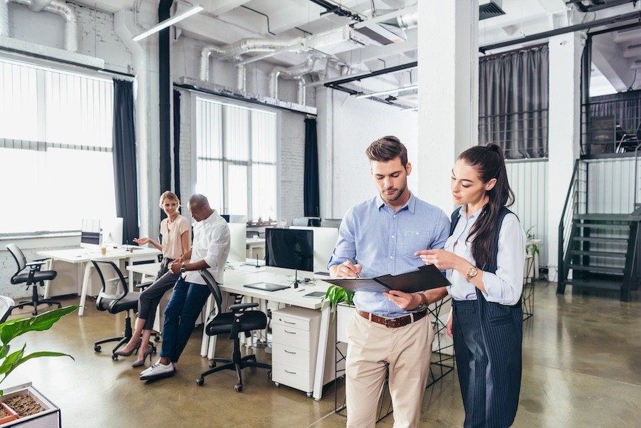  An open-concept office with two pairs of employees discussing different things.