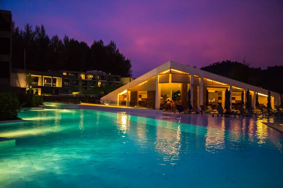 A backyard with a large pool and people sitting outside at dusk.